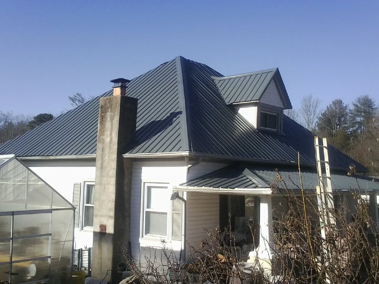 Dark blue standing seam metal roof on a white farmhouse with dormer — Slate & Tile Roof Repair by Roofing Brothers in Buda