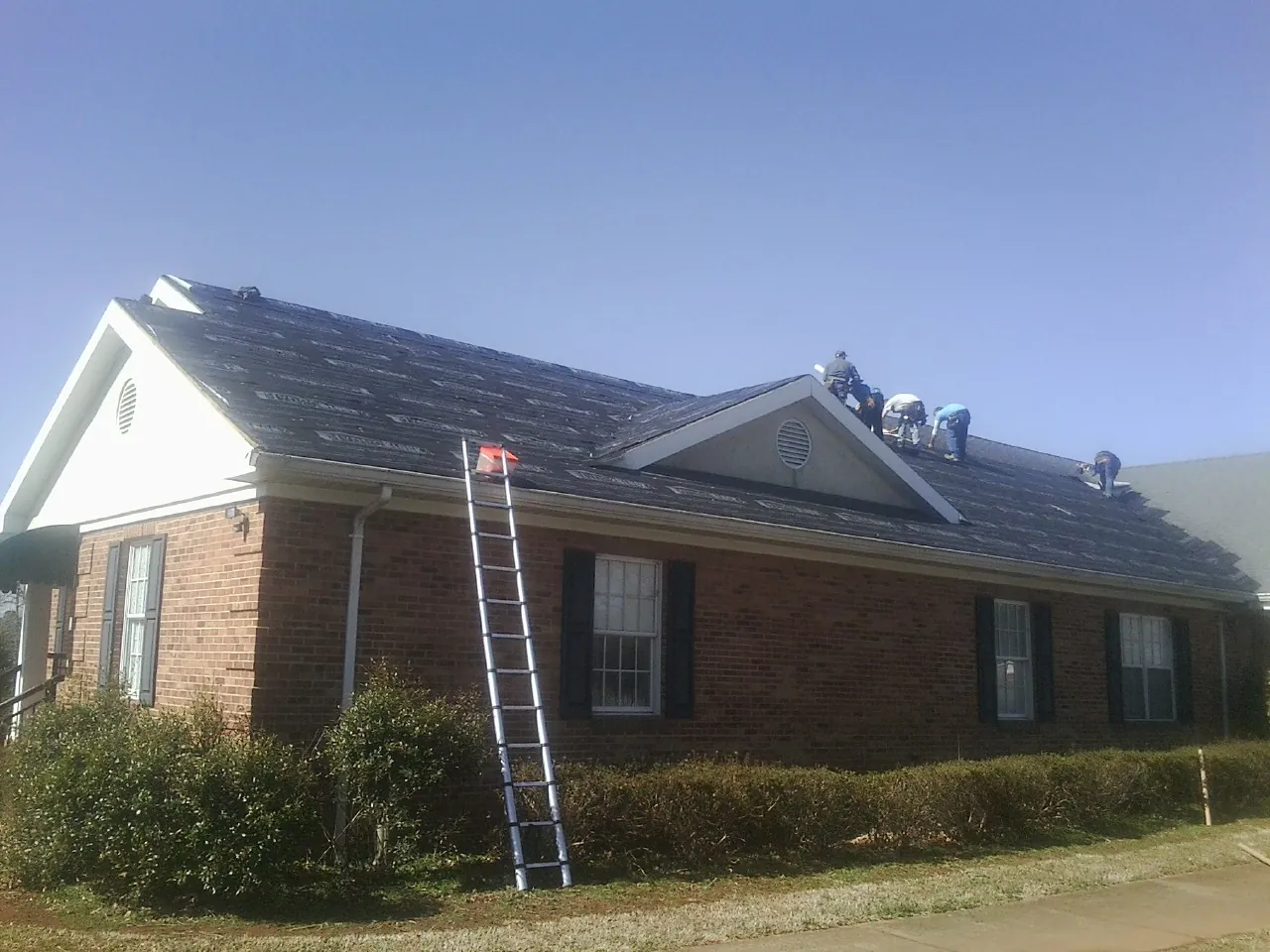 Crew tearing shingles off a brick ranch roof with a ladder set — Emergency Roof Repair work by our crew in Buda