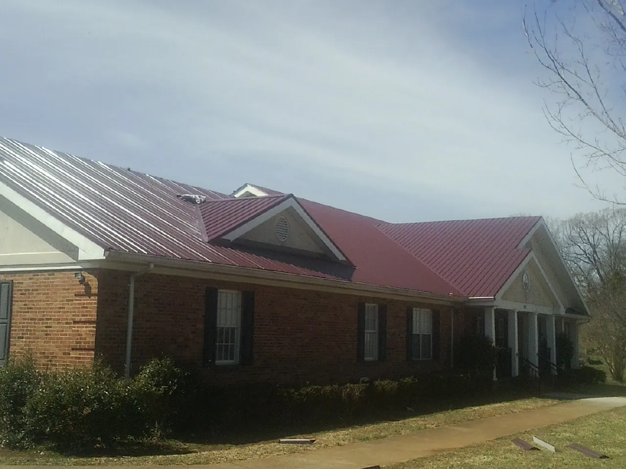 Red metal roof with gabled entries on a long brick building, from a Hail Damage Roof Repair job in Buda