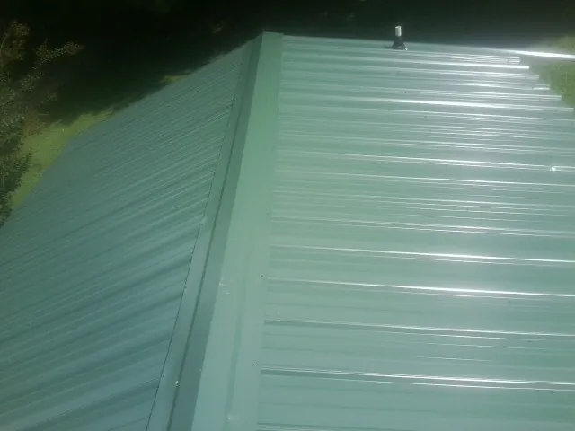 New green metal panels meeting at the ridge of a roof — Flat Roof Repair work by our crew in Buda
