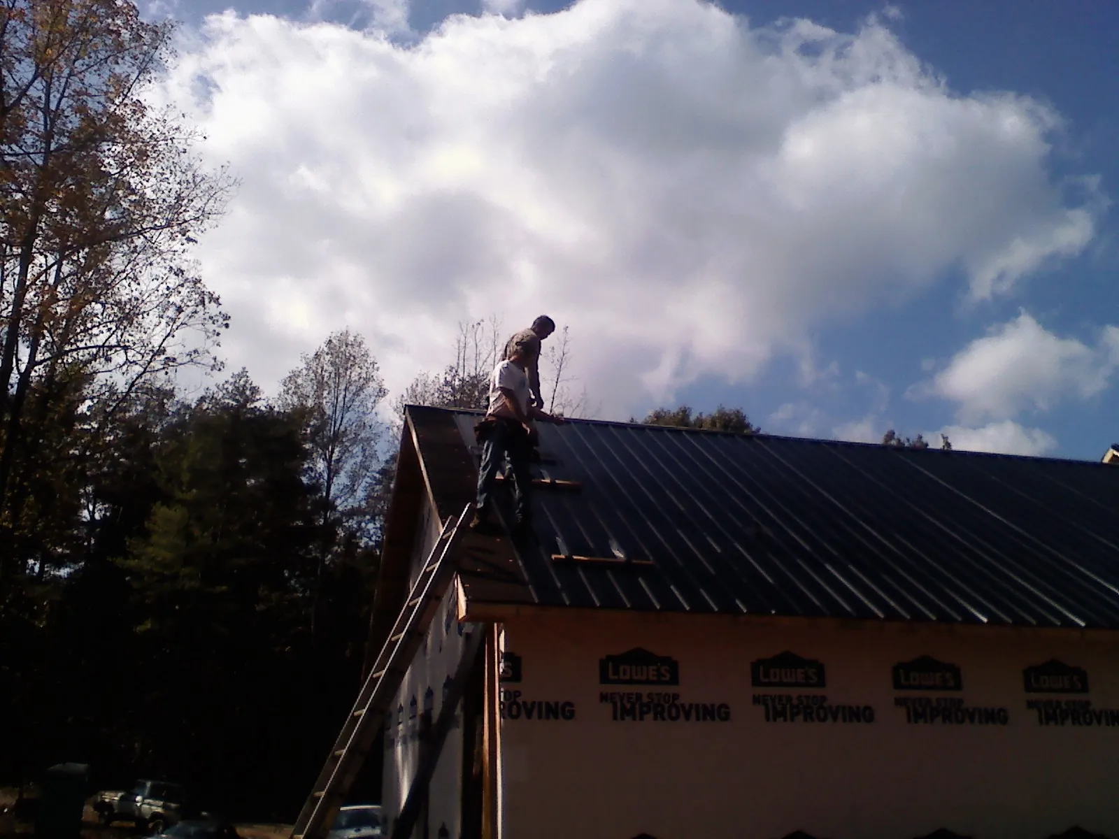 Roofer fastening dark metal panels high against a cloudy sky, from a Roof Inspection job in Buda